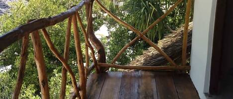 A wooden deck with a thatched roof, surrounded by lush greenery.