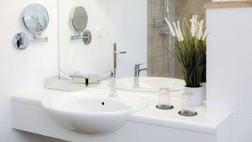 A modern bathroom with a white sink, two round mirrors, a glass shower enclosure, and a potted plant.