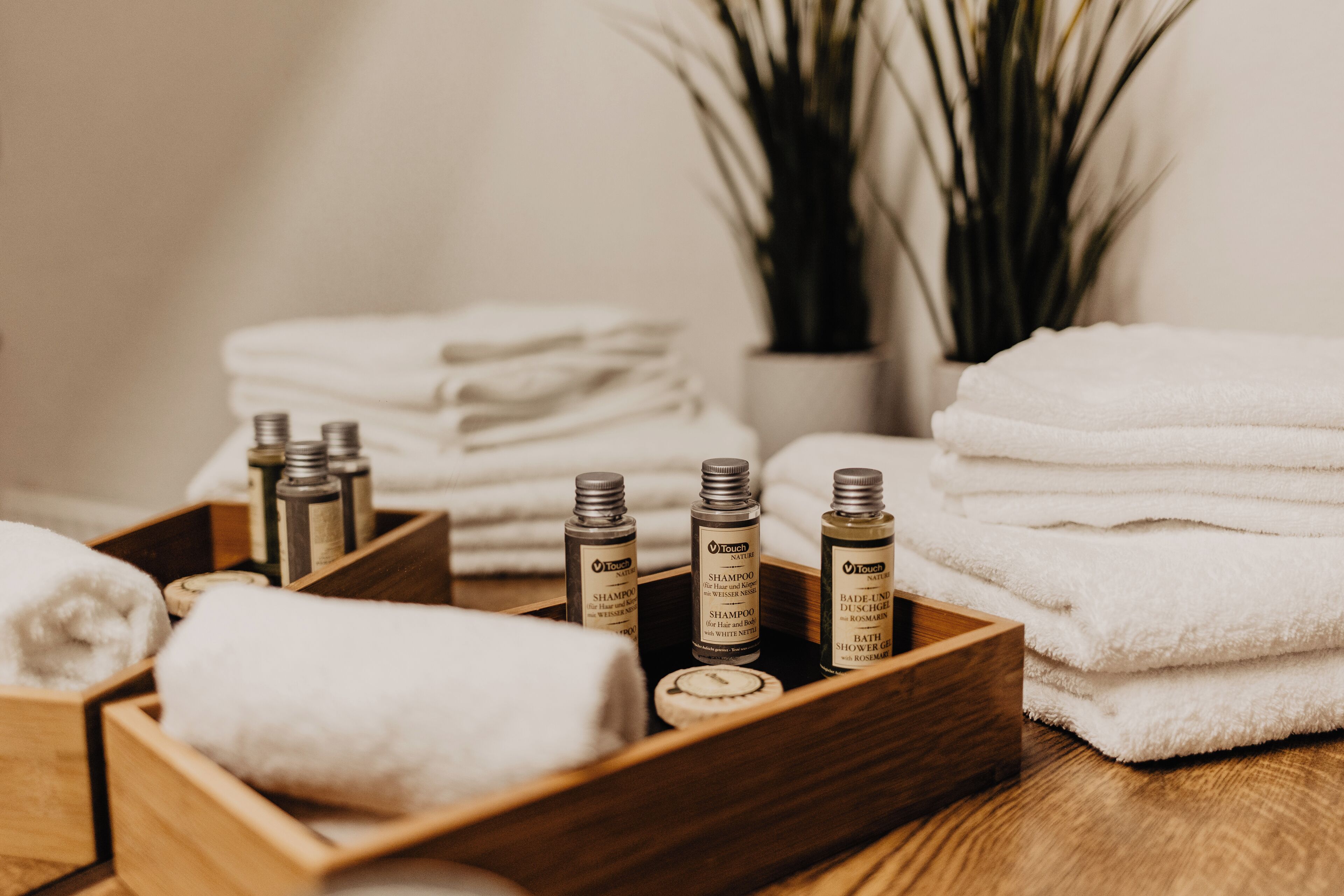 A wooden tray with neatly folded white towels, a bottle of shampoo, and a bottle of bath foam.