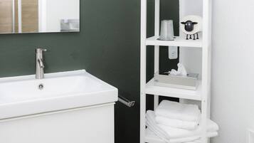 A bathroom with a white sink, a mirror, a white shelf with toiletries, and a hanging plant.