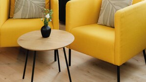 Una habitación con dos sillones amarillos, una mesita redonda con un florero, una lámpara de pie y vistas a través de cortinas de gasa.
