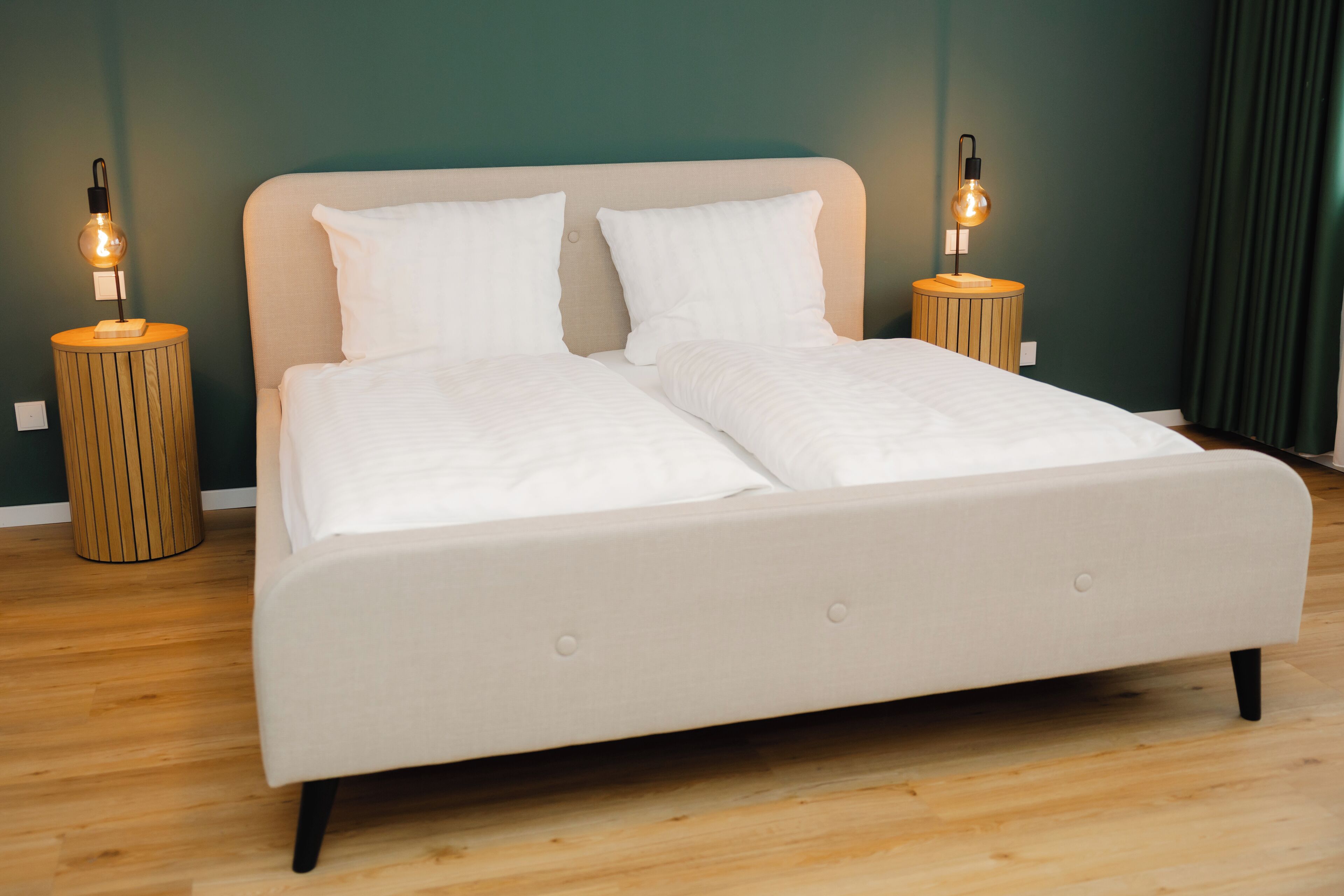 Una cama con dos almohadas blancas y un cabecero color beige, flanqueada por dos mesitas de noche de madera con lámparas.