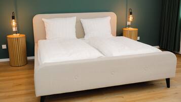 Una cama con dos almohadas blancas y un cabecero color beige, flanqueada por dos mesitas de noche de madera con lámparas.