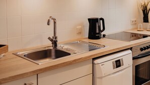 Una cocina moderna con armarios blancos, un lavamanos de acero inoxidable, una cafetera y un lavavajillas.