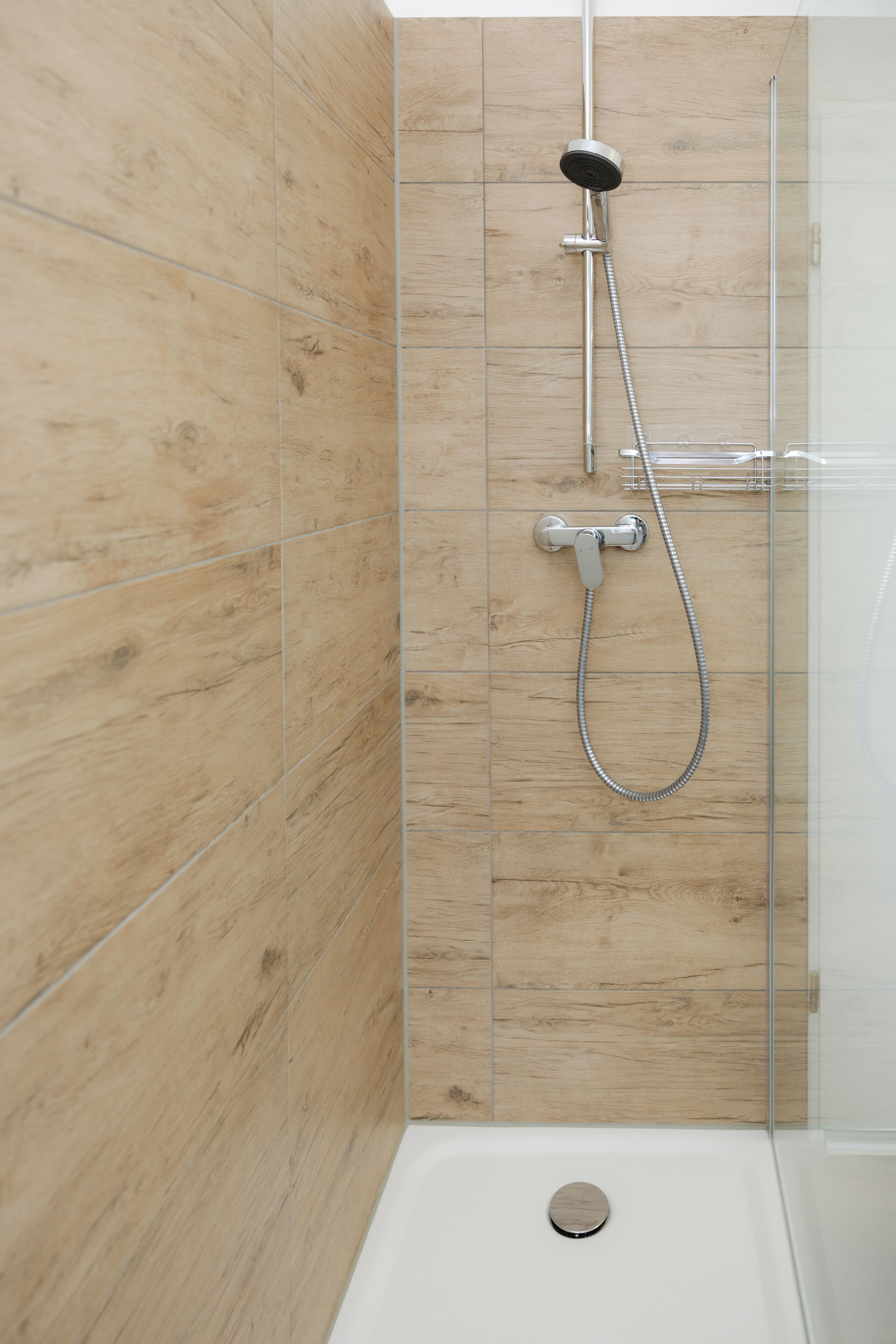 A shower with a handheld showerhead and a wall-mounted faucet, set against a wooden panel wall.