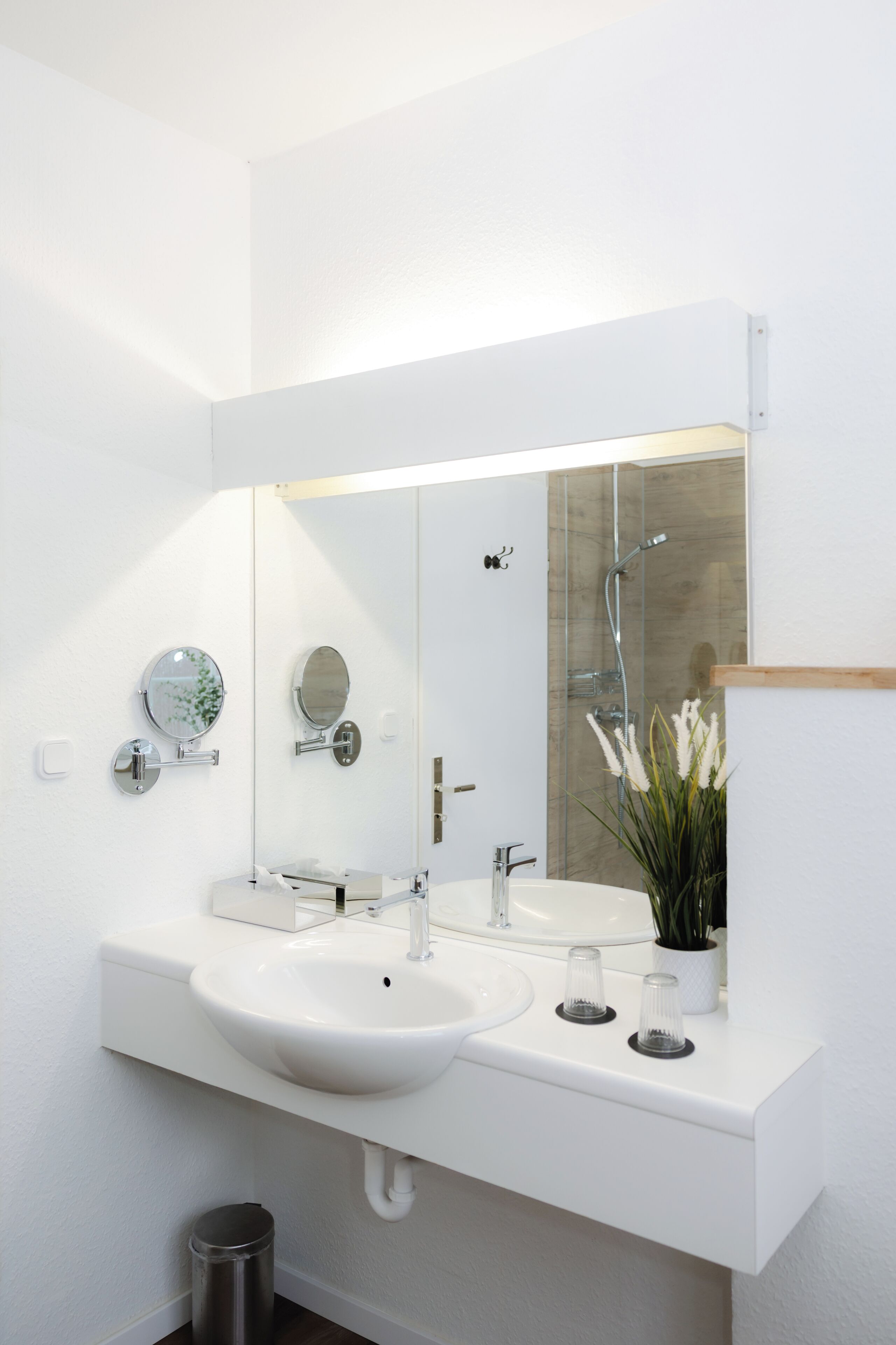 A modern bathroom with a white sink, a large mirror, and a shower.