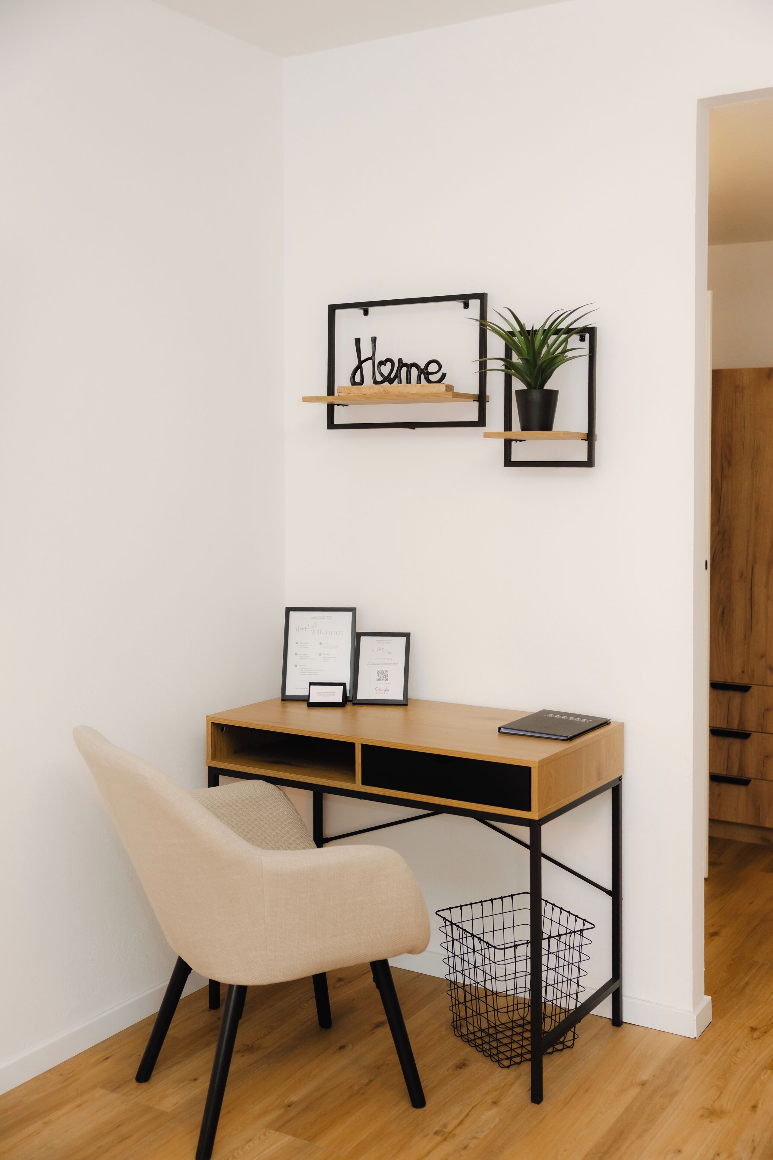 Une pièce d’angle comprenant un bureau, une chaise et des étagères murales où sont exposés des certificats encadrés et une plante en pot.