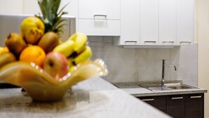 A kitchen with white cabinets, a granite countertop, and a fruit bowl with various fruits.
