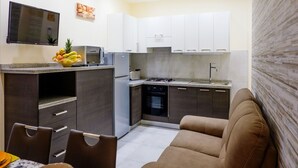 A modern kitchen with white cabinets, a microwave, a toaster, and a stove. There is a dining area with a brown sofa and a table with chairs.
