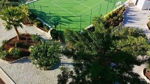 An aerial view of a tennis court surrounded by landscaped gardens and a white building.