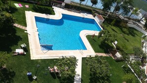 A swimming pool with a diving board, surrounded by a well-maintained lawn and a tennis court in the background.