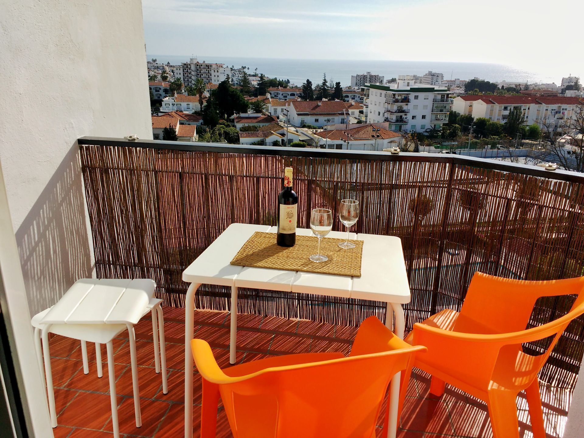 Un balcon avec une table dressée pour deux personnes, une bouteille de vin et deux verres. Le balcon offre une vue sur le paysage urbain de la côte.