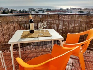 Un balcón con una mesa, dos sillas naranjas, una botella de vino y dos copas.