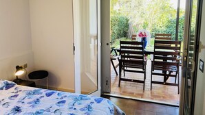 Una camera da letto con un letto, un comodino e una panca da notte. C'è una porta scorrevole in vetro che dà su un patio esterno con tavolo e sedie.