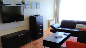 Een moderne woonkamer met een flatscreen televisie, een zwarte bank, een rode fauteuil, een salontafel en een zwarte kast.