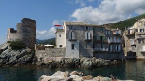 A coastal town with a historic stone tower, a white building with multiple windows, and a red umbrella on the roof.