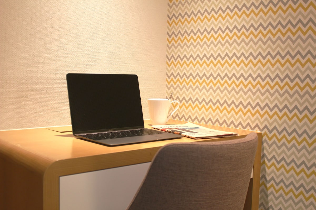 Un ordinateur portable sur un bureau en bois, avec un carnet et une tasse.