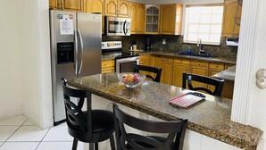 A kitchen with granite countertops, wooden cabinets, stainless steel appliances, and two bar stools.