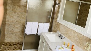 Une salle de bain avec une porte de douche en verre, un lavabo avec des articles de toilette et un miroir.