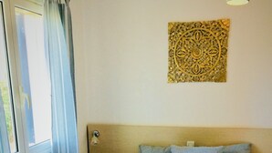 Une chambre à coucher comprenant un lit, une tête de lit, une fenêtre avec des rideaux, un luminaire fixé au mur et un élément décoratif mural.