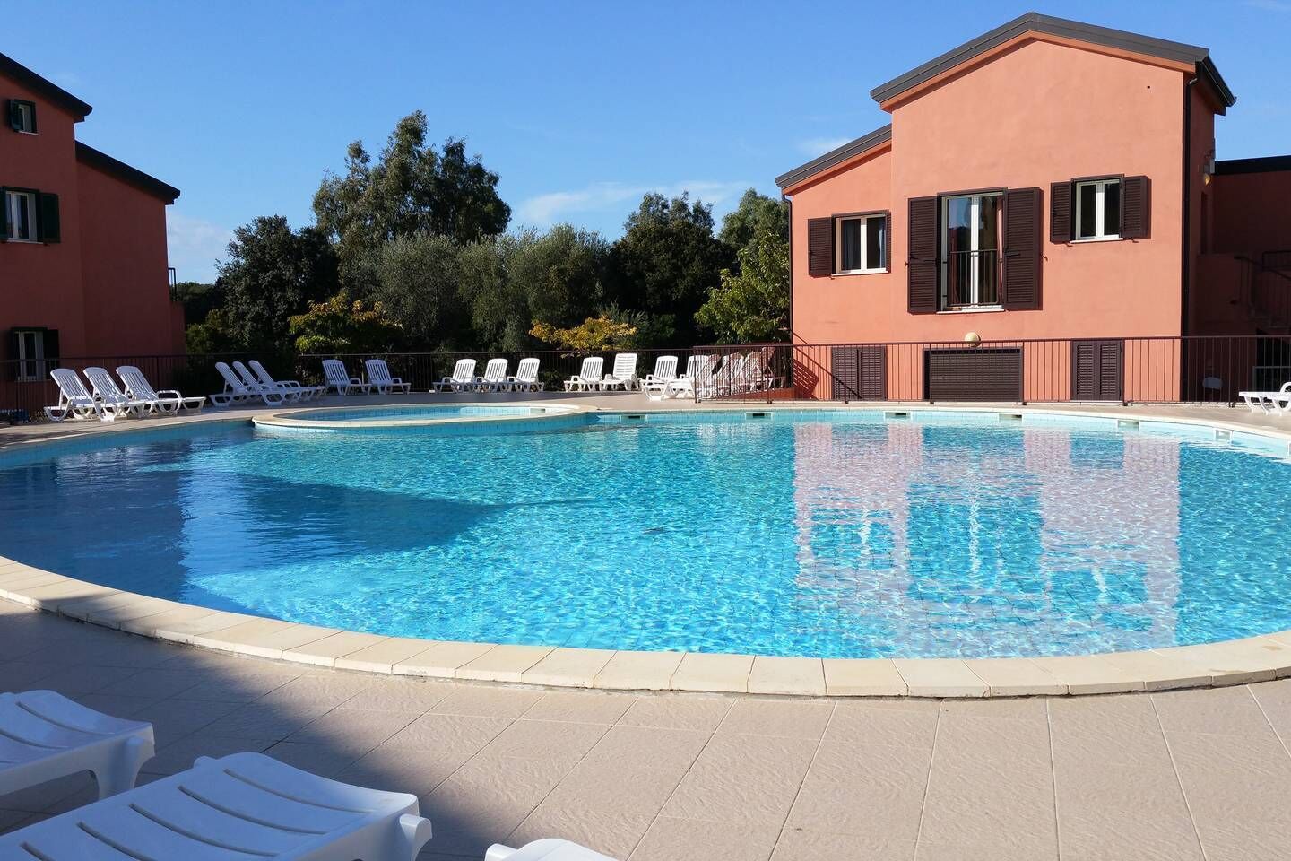 Una piscina con sillas de descanso y un edificio con persianas.