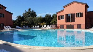 Une piscine avec des chaises longues et un bâtiment doté de volets.