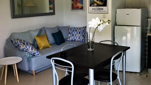 Un espace de vie moderne comprenant un coin repas, un canapé agrémenté de coussins à motifs, une table avec des chaises, un réfrigérateur et un luminaire suspendu.