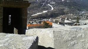 Une construction en pierre offrant une vue sur une montagne enneigée, une route sinueuse et une ville avec des bâtiments situés dans la vallée.