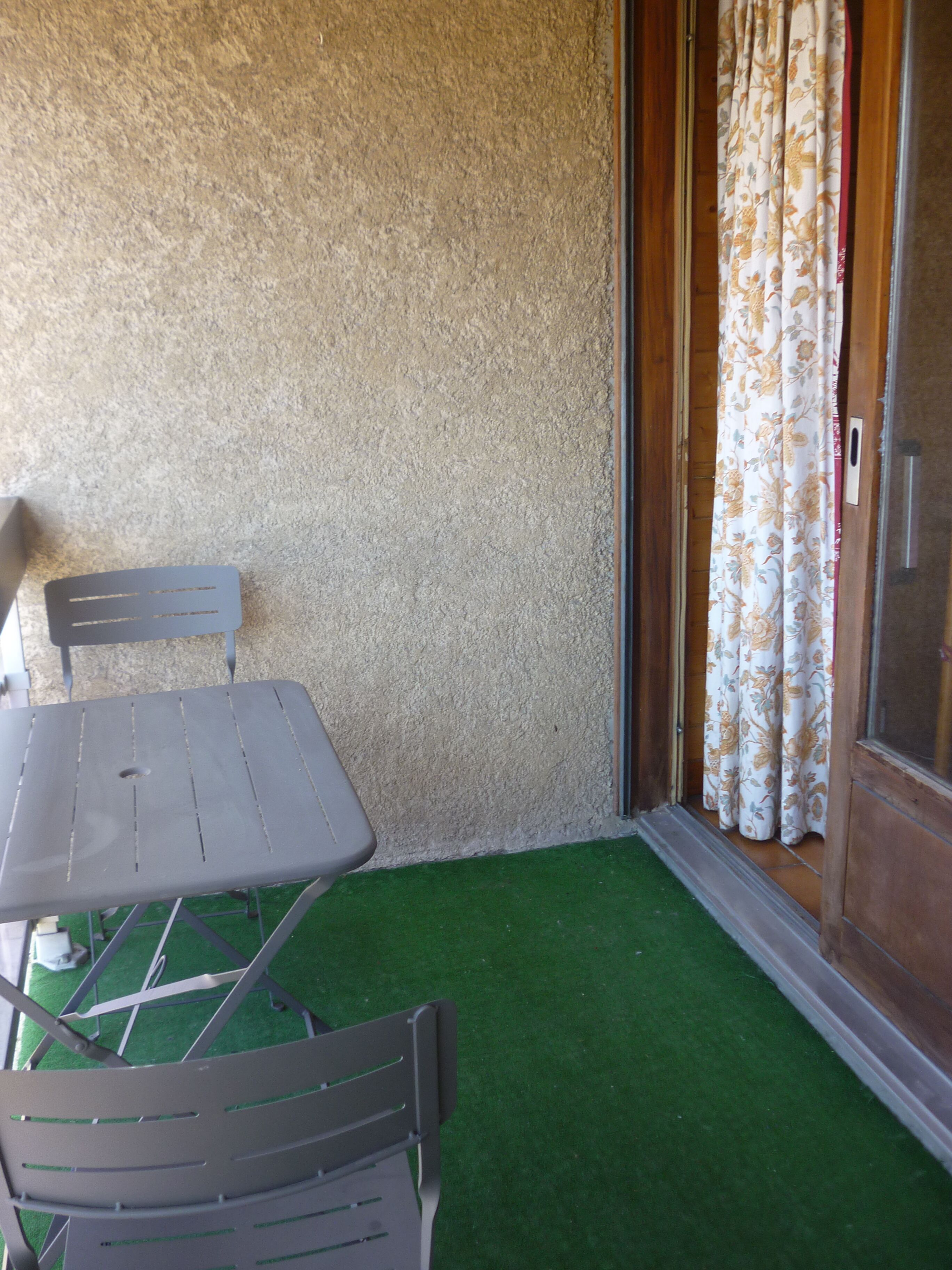 A balcony with a table and chairs, a textured wall, and a door with floral curtains.
