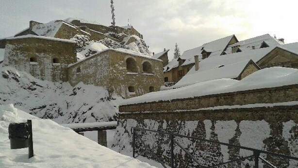 Un bâtiment enneigé, doté d’une façade en pierre et de nombreuses fenêtres, entouré de neige.