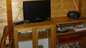 Un intérieur en bois avec une télévision, une radio et une petite table sur laquelle se trouvent des livres et un jeu de Monopoly.