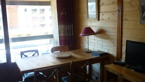 L’intérieur d’un chalet en bois comprend une table à manger, des chaises, un téléviseur et une fenêtre avec des rideaux.