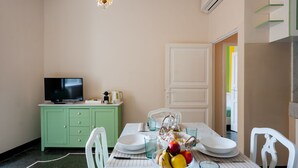 A dining area with a table set for four, a television on a green cabinet, and a door leading to another room.
