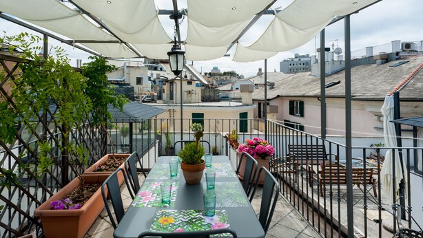 A rooftop terrace with a table set for dining, surrounded by potted plants and a view of the cityscape.
