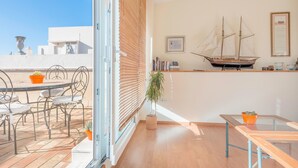 Una habitación con balcón, una mesa de comedor con sillas, una planta en maceta y un modelo de barco en la pared.