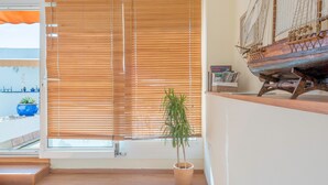 Una habitación con un gran ventanal con persianas, una planta en maceta y un modelo de barco en una estantería.