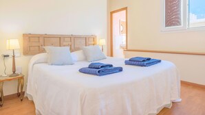 Una cama bien hecha con sábanas blancas y toallas azules, cabecera de madera, lámparas de noche y una ventana con vistas.
