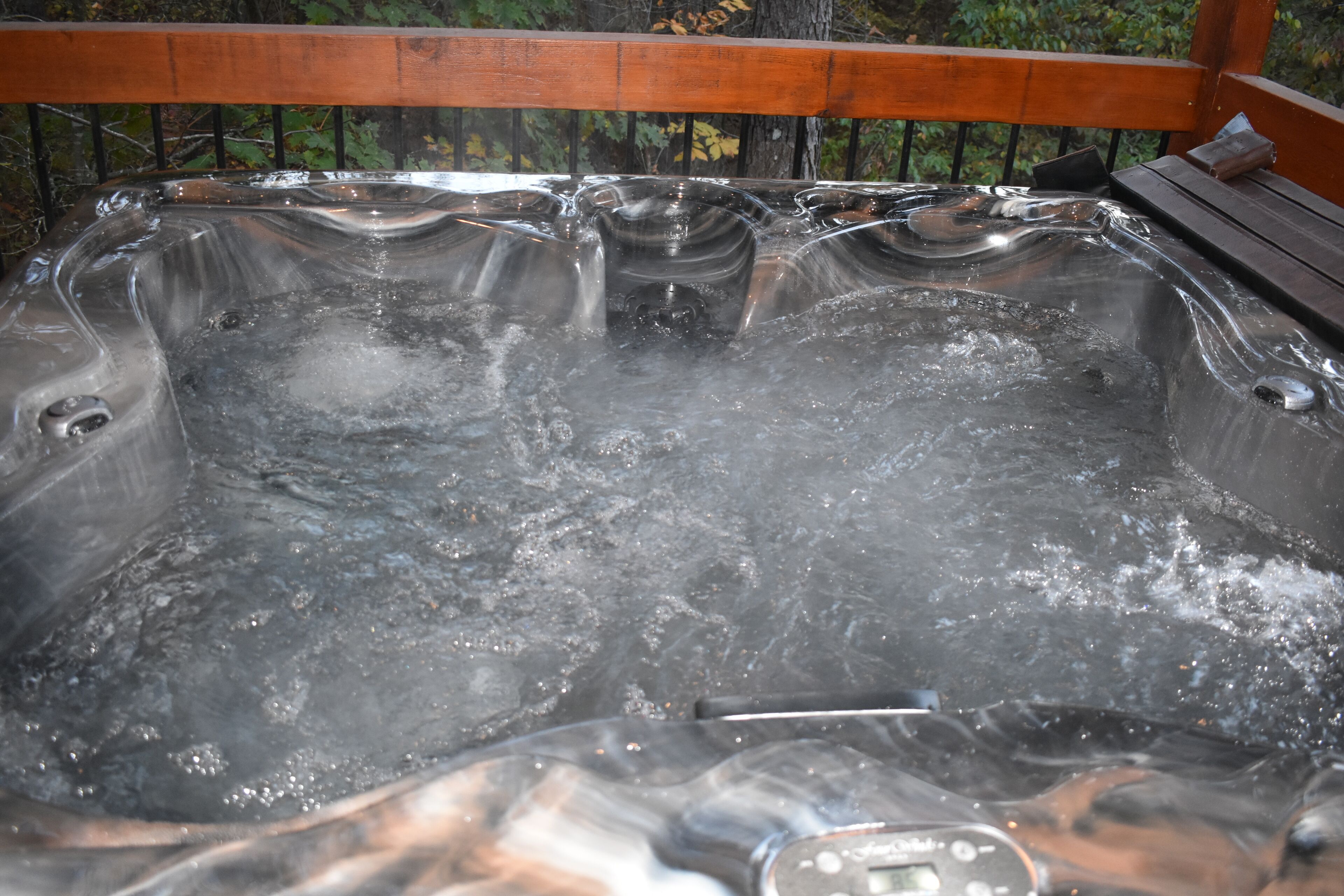 A hot tub with a wooden deck and metal railing.