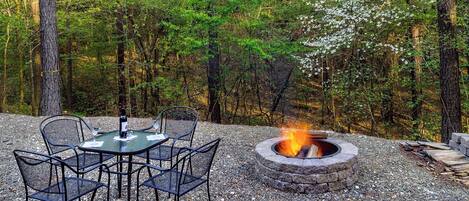 A fire pit surrounded by a gravel area with metal chairs and a table.
