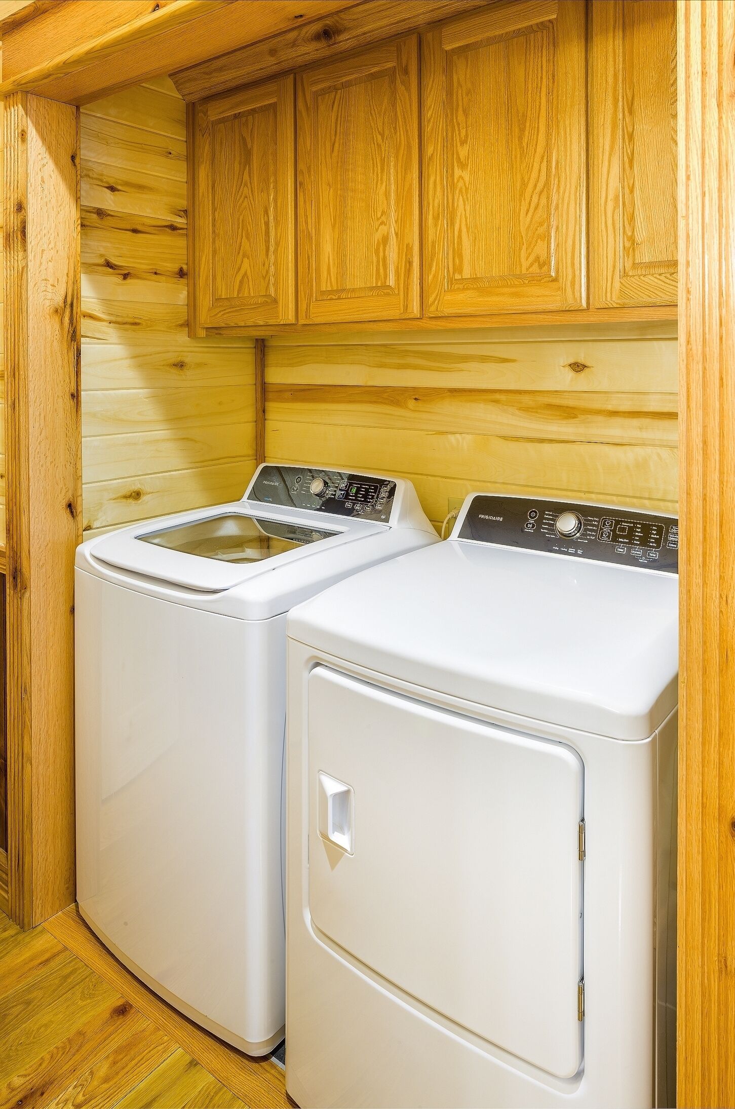 A laundry room with two front-loading washing machines and wooden cabinets.
