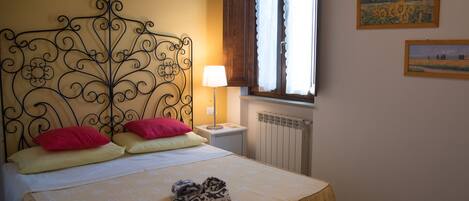 A bedroom with a bed, a window with curtains, a radiator, and a framed picture on the wall.