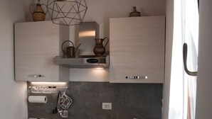 A modern kitchen with a gas stove, sink, and a wooden table with bread and cups. - Villa Tresino apartments "Velia" (Alani)
