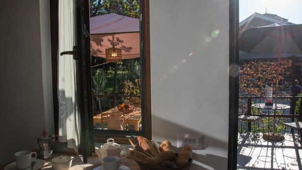 A dining area with a table set for tea, a basket of bread, and a view of an outdoor patio with umbrellas. - Villa Tresino apartments "Velia" (Alani)