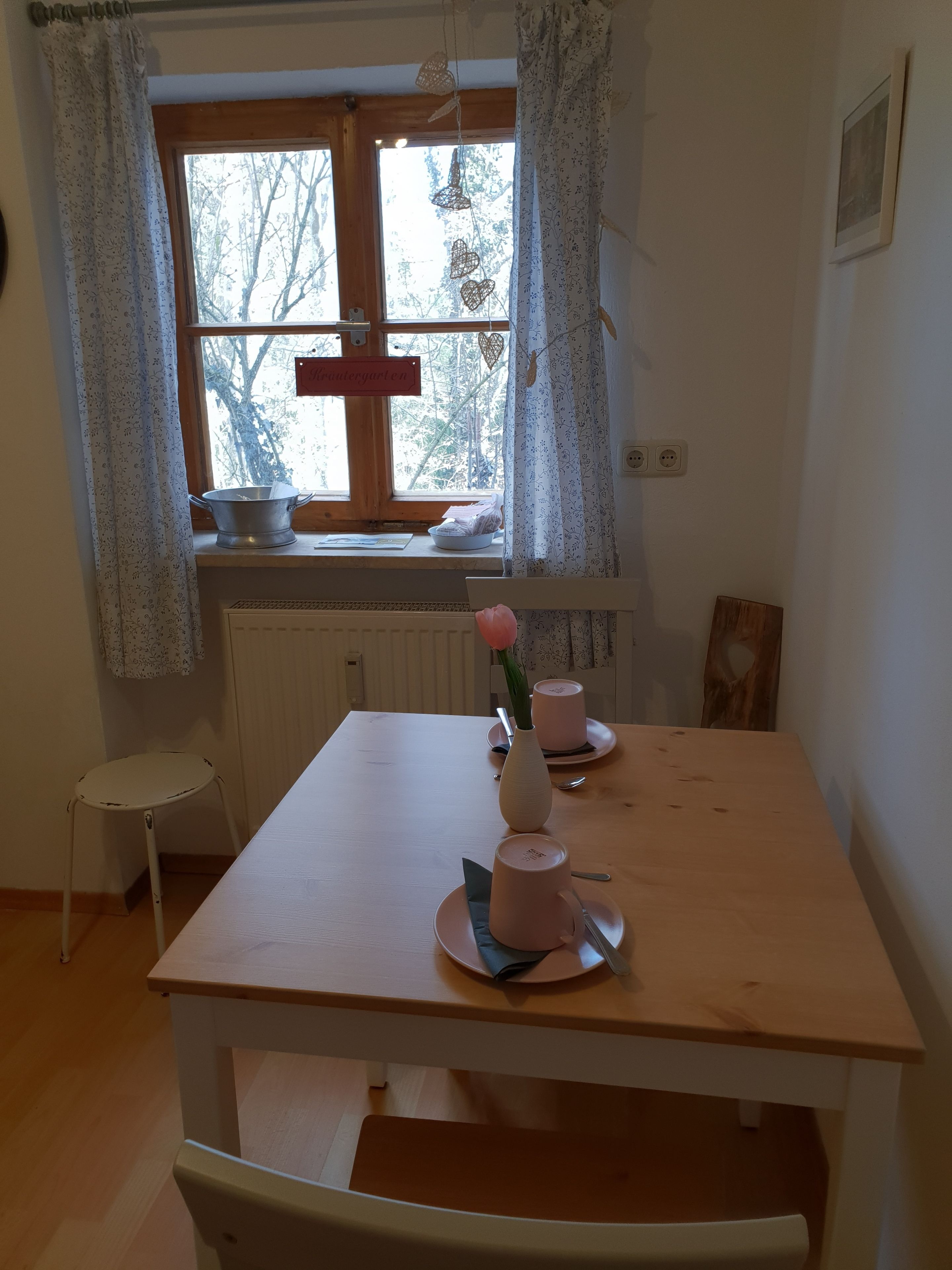 Ruokailutila, jossa on puinen pöytä, vaasi, jossa on vaaleanpunainen kukka, ja ikkuna, jossa on verhot.