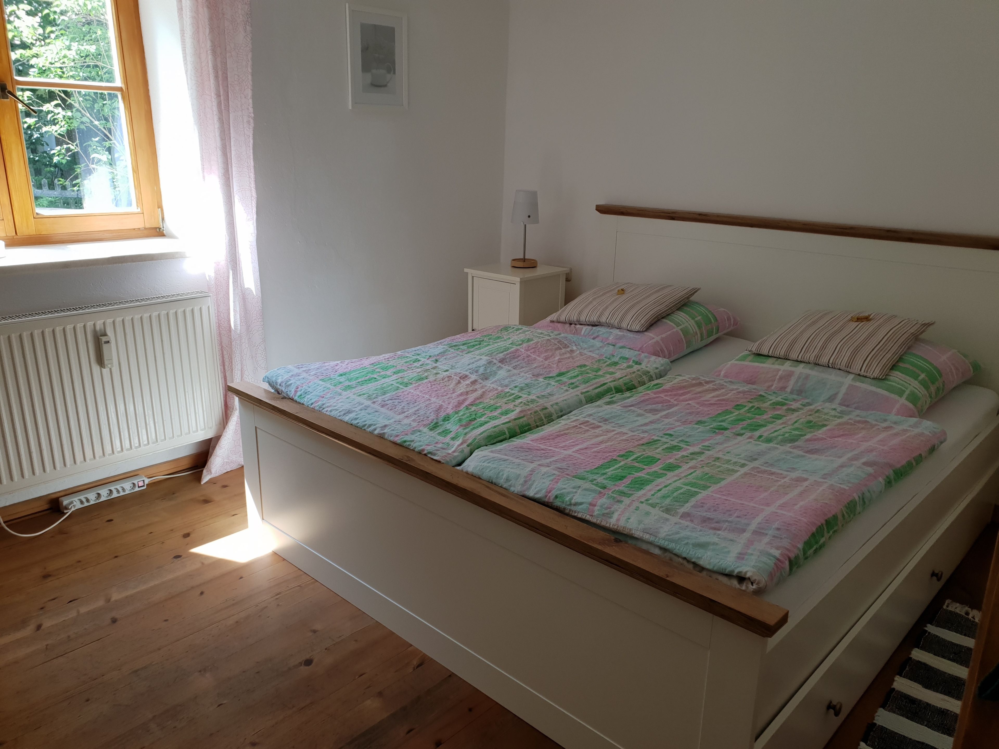 Ein Schlafzimmer mit einem hölzernen Bett, weißen Wänden, einem Fenster mit Vorhängen und einer Heizung.