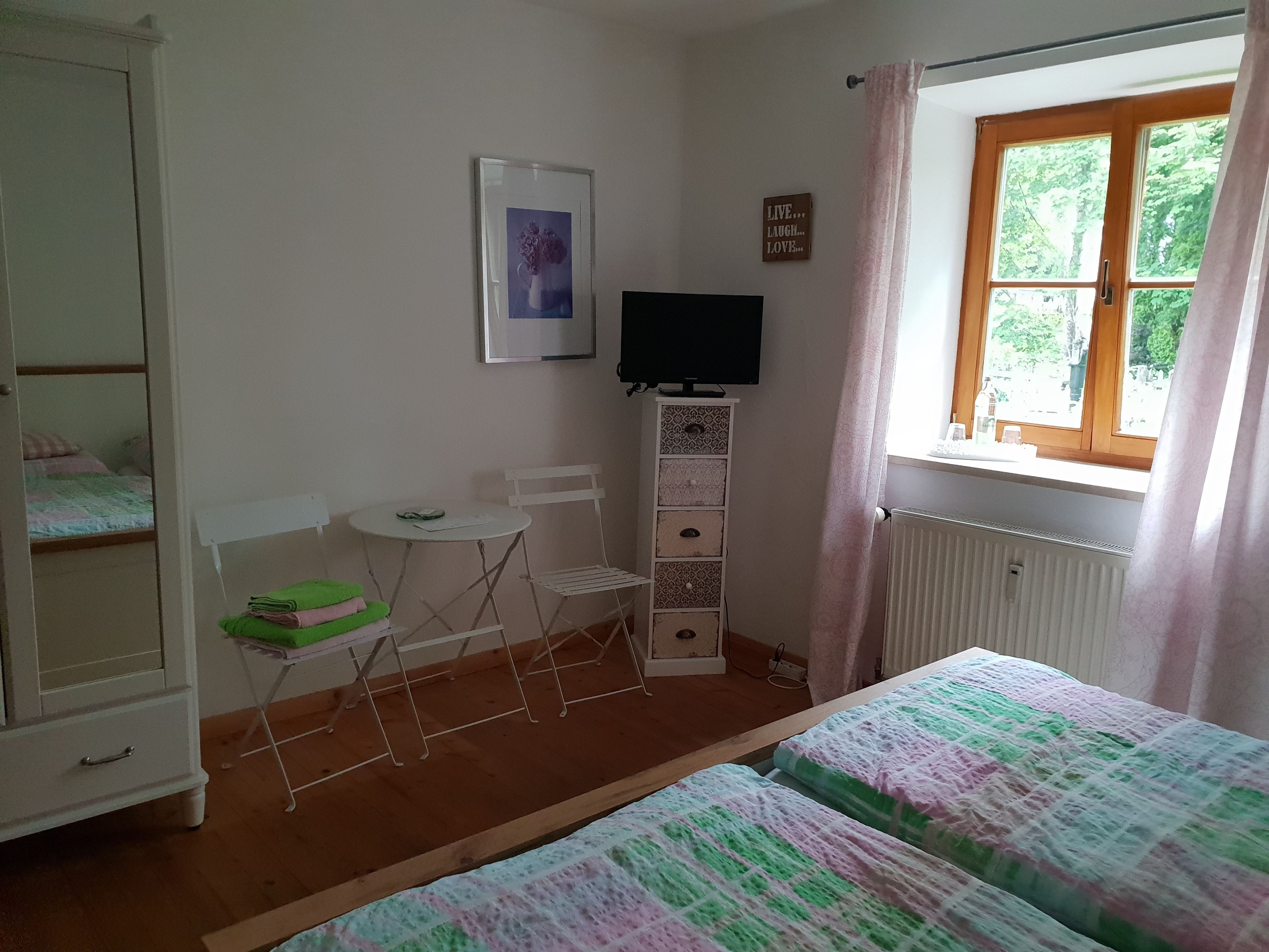 Camera da letto con due letti, un tavolino, una sedia, una TV e una finestra con tende.