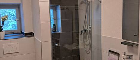Une salle de bain moderne avec une douche à parois de verre, des toilettes blanches et un lavabo avec un miroir au-dessus.