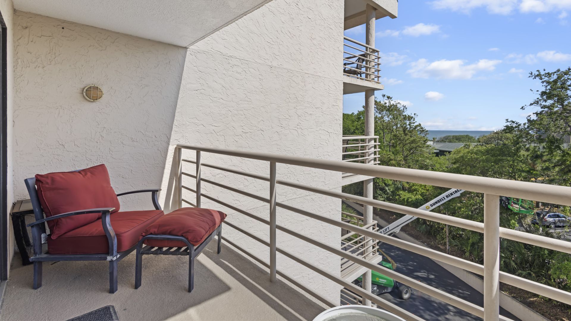 Un balcon avec une chaise rouge, une rambarde en métal et une vue sur une route et la verdure.