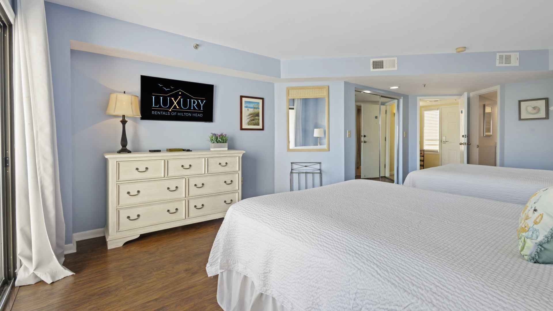 A bedroom with two beds, a dresser, a mirror, and a sign advertising luxury rentals.