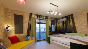 A hotel room with a brick wall, a sofa with colorful cushions, a bed with white linens, and a large window with curtains.